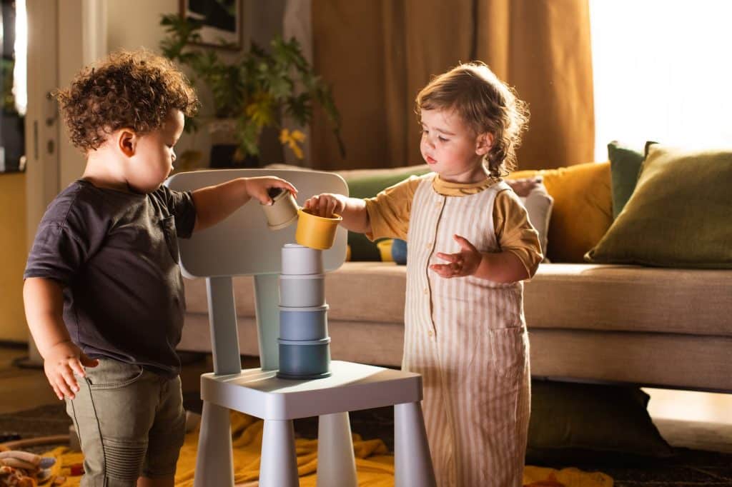 Two children playing with a stacking chair in a living room.